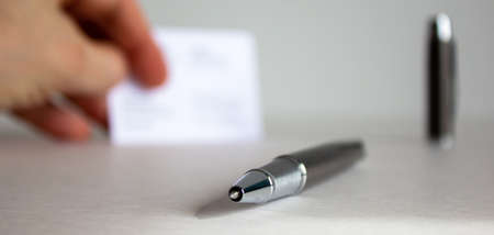 Pen on beautiful white fon on warm light. Fingers with visit cards and cap in the background.の写真素材