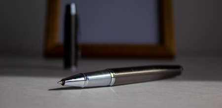 Pen on beautiful white fon on warm light. Wooden picture frame and cap in the background.の写真素材