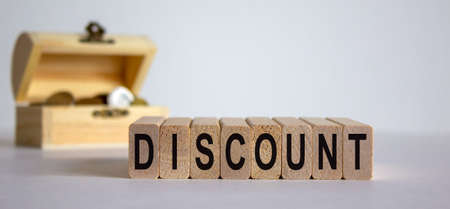 Concept word 'discount' on wooden blocks on a beautiful white background, small chest with coins.の写真素材