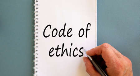 Hand writing 'Code of ethics' on white note, isolated on blue background.の写真素材