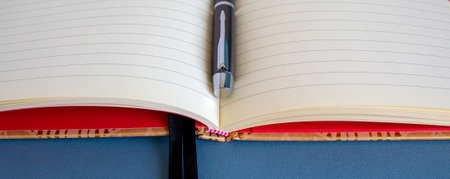 Open notebook and black beautiful pen on blue background.の写真素材