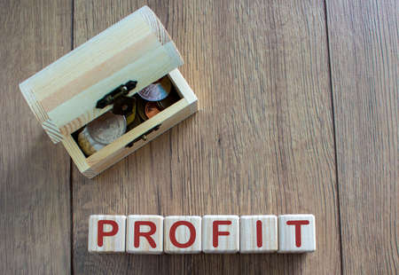 Concept word profit on cubes on a beautiful wooden table, small chest with coins.
