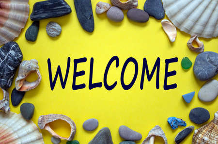 Word 'welcome' on a beautiful yellow background. Sea stones and seashells. Concept.