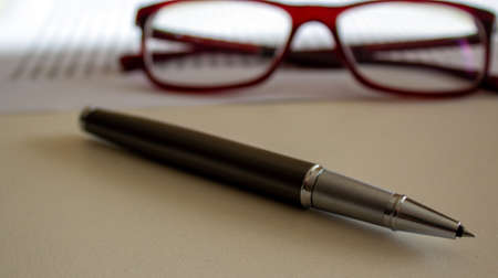 Metal pen and beautiful glasses on white document on a white table. Business concept.の写真素材