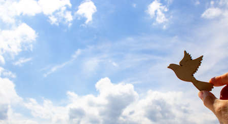Man hand holding wooden bird on cloud sky background. The development of the imagination, copy space.の写真素材