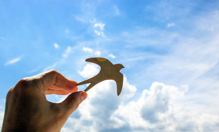 Man hand holding wooden bird on cloud sky background. The development of the imagination, copy space.の写真素材