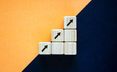 Business concept growth success process. Wood block with arrow signs stacking as step stair on paper peach and black background, copy space.の写真素材