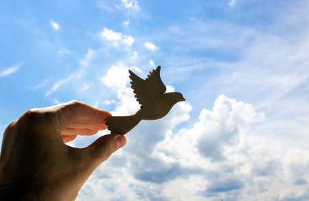 Man hand holding wooden bird on cloud sky background. The development of the imagination, copy space.の写真素材