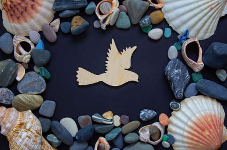 Wooden bird on a beautiful black background. Sea stones and seashells. Concept.の写真素材