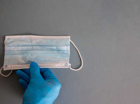 Doctors hand in blue glove with medical protection mask on blue background. Medical and COVID-19...