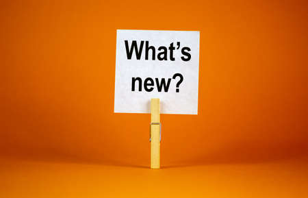 White paper with text 'Whats New', clip on wood clothespin. Beautiful orange background. Business concept. Copy space.の写真素材