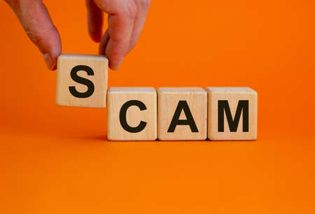 Concept word 'scam' on cubes on a beautiful orange background. Male hand. Business concept. Copy space.の写真素材