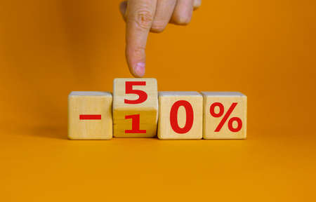 Hand turns a cube and changes the expression '-10 percent' to '-50 percent'. Beautiful orange background, copy space. Business concept.の写真素材