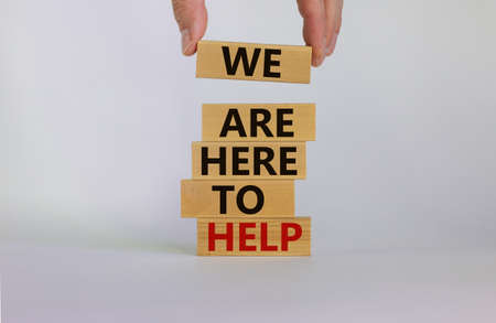 Wooden blocks with text 'we are here to help'. Male hand. Beautiful white background, copy space....