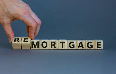 Hand turns cubes and changes the word 'remortgage' to 'mortgage' or vice versa. Beautiful gray background, copy space. Business concept.の写真素材