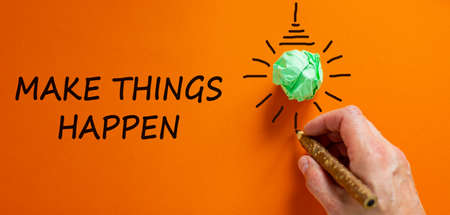 Male hand writing a 'Make things happen' sign next to a light bulb shape over orange background. Copy space. Business concept.の写真素材