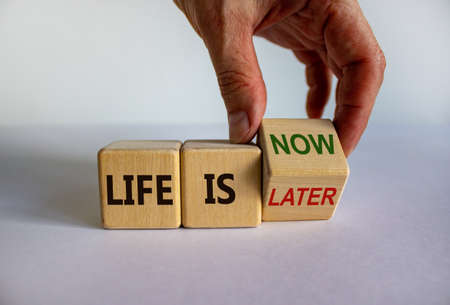 Hand turns a cube and changes the expression 'life is later' to 'life is now'. Beautiful white...