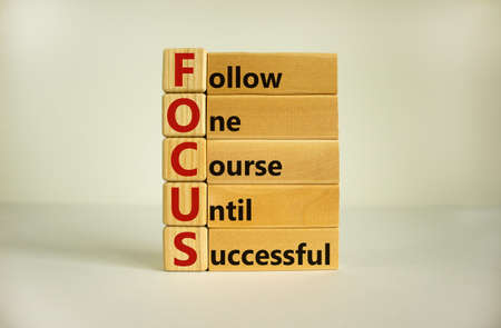 Wooden cubes and blocks with words 'FOCUS, follow one course until successful'. Beautiful white background, copy space. Business concept.