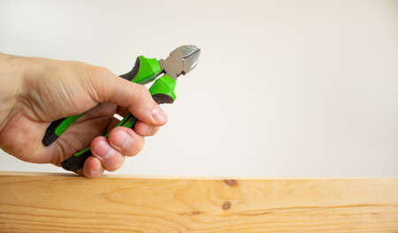 A male hand holds a wire cutters on a wooden bar. Beautiful white background. Copy space. Concept.