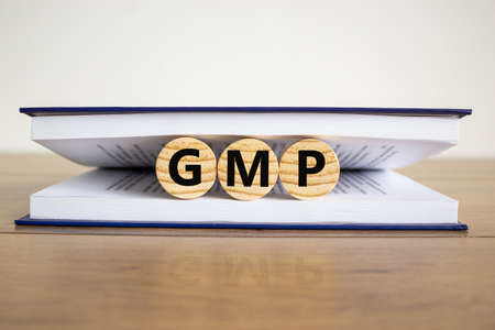 Concept word 'GMP, good manufacturing practice' on wooden circles between pages of a book on a beautiful wooden table. White background. Business concept, copy space.の写真素材