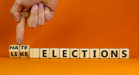 Hate or like elections. Male hand flips wooden cubes and changes the inscription 'like elections' to 'hate elections' or vice versa. Beautiful orange background, copy space.の写真素材
