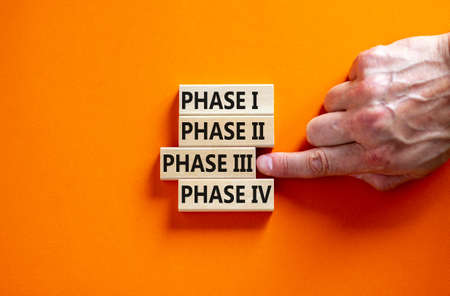 Time to phase 3. Wooden blocks form the words 'phase, 1, 2, 3, 4' on orange background. Male hand. Beautiful background. Business and covid-19 vaccine trial concept.の写真素材