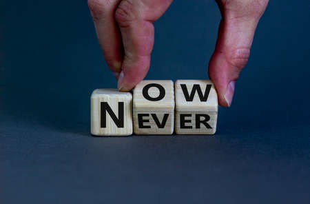 Now or never. Male hand flips wooden cubes and changes the inscription 'never' to 'now' or vice versa. Beautiful gray background, copy space.の写真素材