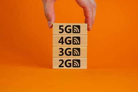 5G network evolution concept. Hand holding a wooden block with text and symbol. Copy space. Beautiful orange background.の写真素材