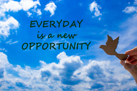 Man hand holding wooden bird on cloud sky background. Words 'everyday is a new opportunity' The development of the imagination, copy space.の写真素材