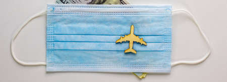 Coronavirus flight cancellations concept. Face mask and airplane toy on white background. Dollar bills. Copy space.の写真素材
