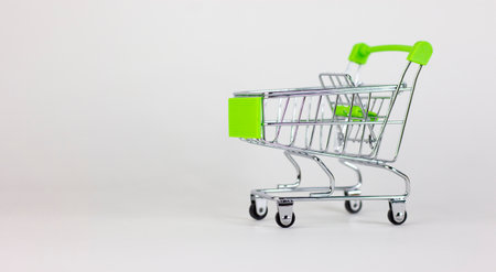 Time to shopping. Empty miniature shopping cart isolated on white. Close-up shot, side view. Beautiful white background, copy space. Shopping concept.の写真素材