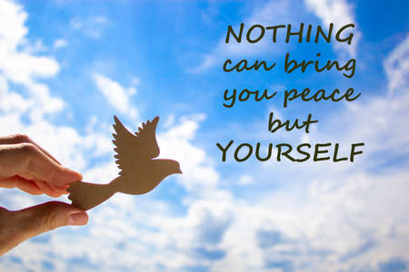 Man hand holding wooden bird on cloud sky background. Words 'nothing can bring you peace but yourself'. The development of the imagination, copy space. Motivational and business concept.の写真素材