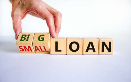 Big or small loan symbol. Businessman turns a wooden cube and changes words 'small loan' to 'big...