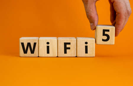 WiFi 5 symbol. Businessman holds a wooden cube with words WiFi 5. Beautiful orange background, copy space. Business, technology and WiFi 5 concept.の写真素材