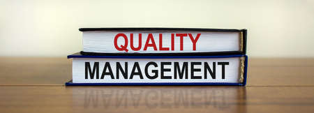 Quality management symbol. Concept words 'Quality management' on books on a beautiful wooden table, white background. Business and quality management concept.の写真素材