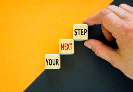 Your next step symbol. Hand arranging wood block stacking as step stair on top with words Your next Step. Business concept for personal ladder of success process. Orange background, copy space.の写真素材