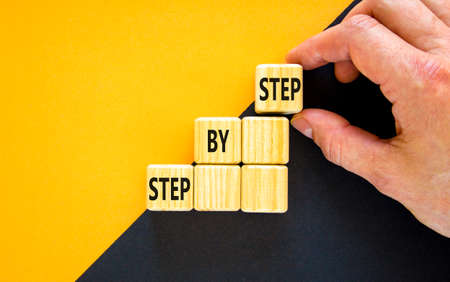 Step by step symbol. Hand arranging wood block stacking as step stair on top with words Step By Step. Business concept for personal ladder of success process. Beautiful yellow background, copy space.の写真素材