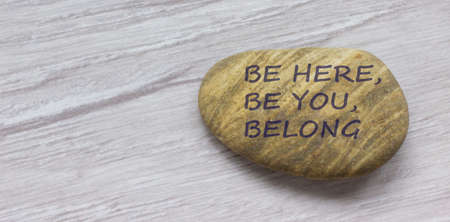 Be here, be you, belong symbol. Beautiful stone with words 'Be here, be you, belong' on beautiful white wooden background. Diversity, business, inclusion and belonging concept.の写真素材