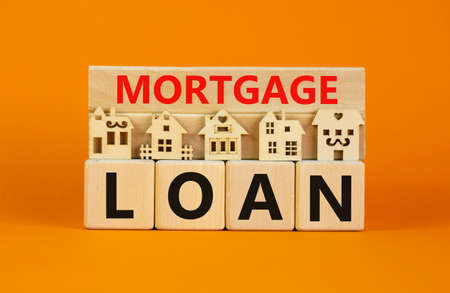Mortgage loan symbol. Models of a wooden house. Words 'mortgage loan' on wooden block. Copy space. Business and mortgage loan concept. Beautiful orange background.の写真素材