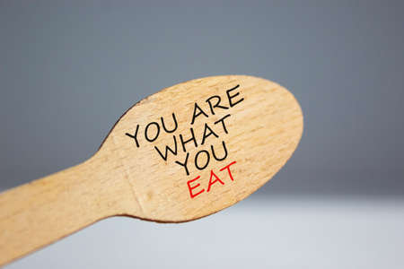 You are what you eat symbol. Wooden spoon on white background. Beautiful warm sunlight. Words 'You are what you eat'. Beautiful white background. Healthy eating concept. Copy space.の写真素材