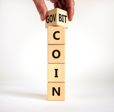 Bitcoin vs govcoin symbol. Businessman turns wooden cubes and changes the word 'bitcoin' to 'govcoin'. Beautiful white table, white background, copy space. Business, bitcoin vs govcoin concept.の写真素材