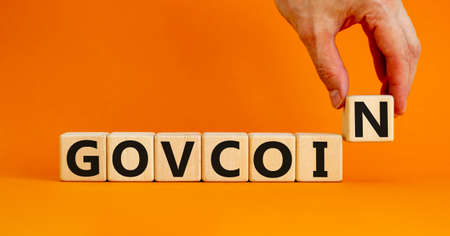 Govcoin symbol. Wooden cubes with the word 'govcoin'. Beautiful orange table, orange background,...