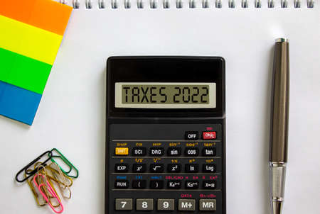 Business concept of taxes planning 2022. Calculator with words 'taxes 2022', metalic pen. Colored paper, paper clips. Business, taxes 2022 concept. Beautiful white background, copy space.の写真素材