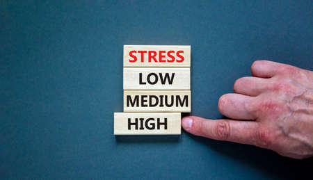 Low or high stress level symbol. Businessman chooses the wooden block with words high stress. Words stress low medium high. Beautiful gray background. Low or high stress level concept. Copy space.の写真素材