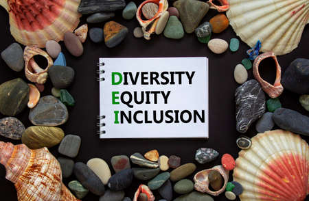DEI, diversity, equity, inclusion symbol. Words DEI, diversity, equity, inclusion on a beautiful white note, black background. Sea stones and seashells. DEI, diversity, equity, inclusion concept.の写真素材