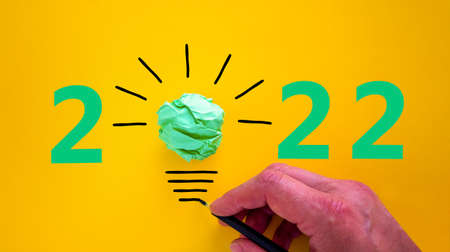 2022 happy new year symbol. Number 2022. Businessman hand with black pen, green light bulb icon. Beautiful yellow background. Copy space. Business and 2022 happy new year concept.の写真素材