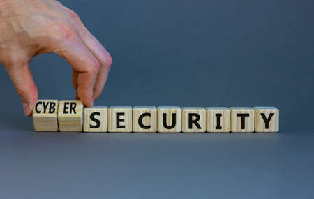 Cyber-security or security symbol. Businessman turns wooden cubes, changes words security to cyber-security. Beautiful grey background. Cyber-security and security concept. Copy space.の写真素材