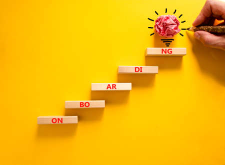 Onboarding success symbol. Wooden blocks with the word Onboarding. Beautiful yellow background, copy space. Businessman hand, light bulb. Business, Onboarding success concept.の写真素材