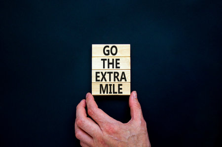 Go the extra mile symbol. Concept words Go the extra mile on wooden blocks. Businessman hand. Beautiful black table, black background, copy space. Business and go the extra mile concept.の写真素材