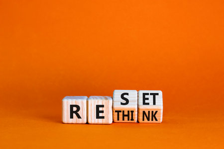 Rethink and reset symbol. Turned wooden cubes and changed the concept word Rethink to Reset. Beautiful orange table orange background. Business rethink and reset concept. Copy space.の写真素材